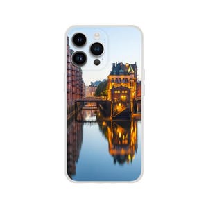 Puede incluir: Una funda para teléfono con una foto de un edificio con un puente y agua delante. El edificio está iluminado por la noche y se refleja en el agua.