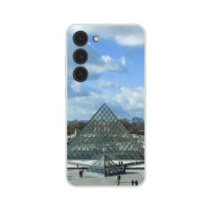 May include: A glass pyramid structure with a blue sky and white clouds in the background. There are people walking around the pyramid.