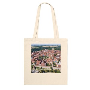 Op de afbeelding: Een witte canvas tas met een kleurrijke luchtfoto van een stad met rode daken en de tekst "ROTHENBURG ODT" gedrukt op de voorkant.