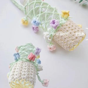 May include: Two handmade crochet water bottle holders. One is light green with a handle and a net-like design, adorned with colorful crochet flowers. The other is cream-colored with yellow trim and similar floral accents.
