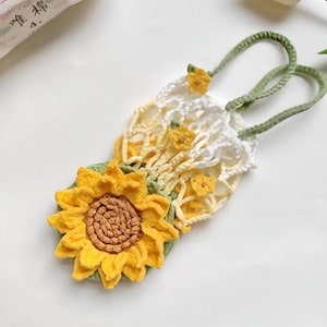 May include: A handmade crochet bookmark featuring a large yellow sunflower with a brown center. The bookmark has a white and yellow net-like design with green handles and accents. The overall design is floral and decorative.