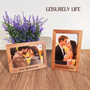 May include: Two wooden photo frames with pictures of couples, one with the text "Our Agreement" and the other with "A memorable day". A purple plant sits behind the frames. The words "LEISURELY LIFE" are at the top.