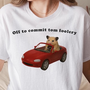 May include: White t-shirt with the phrase "Off to commit tom foolery" in black text. The shirt features a graphic of a red convertible car with a hamster and a dog inside.