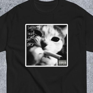 May include: Black and white graphic t-shirt featuring a cat smoking a cigarette with the text "Support Local Street Cats" and a parental advisory label.