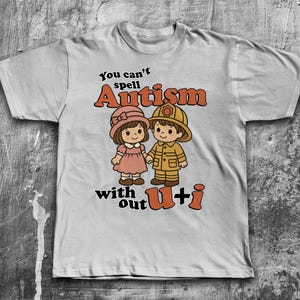 May include: A grey t-shirt with a graphic of two cartoon children and the text "You can't spell Autism without U+i".