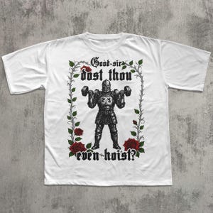 May include: White t-shirt featuring a black and white illustration of a knight lifting dumbbells. The design includes the text "Good-sir dost thou even hoist?" framed by roses and vines. A unique graphic tee for fitness enthusiasts.