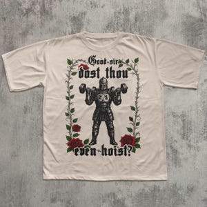 May include: Cream-colored t-shirt featuring a black illustration of a knight lifting dumbbells. The knight is surrounded by a floral border with red roses and the text "Good sir dost thou even hoist?" in gothic lettering.