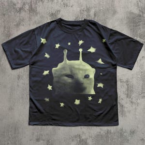 Puede incluir: Camiseta azul marino oscuro con un dise&ntilde;o de extraterrestre verde claro y estrellas. El dise&ntilde;o es de semitonos. La camiseta tiene cuello redondo y mangas cortas. La camiseta es de material suave.