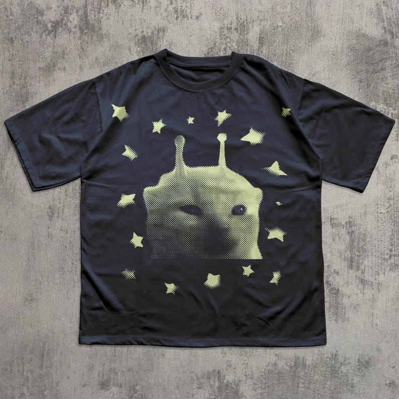 Puede incluir: Camiseta azul marino oscuro con un dise&ntilde;o de extraterrestre verde claro y estrellas. El dise&ntilde;o es de semitonos. La camiseta tiene cuello redondo y mangas cortas. La camiseta es de material suave.