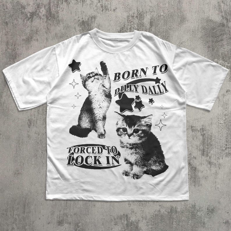 May include: White t-shirt with two monochrome kitten illustrations and the text "BORN TO DILLY DALLY" and "FORCED TO LOCK IN". The design includes star and sparkle graphics.