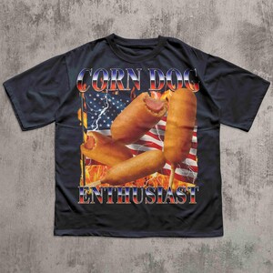 Op de afbeelding: Zwart T-shirt met een afbeelding van corn dogs voor een Amerikaanse vlag met bliksem en vlammen. De tekst "CORN DOG ENTHUSIAST" is in rood, wit en blauw.