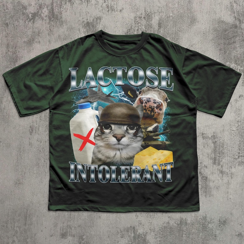 May include: Dark green t-shirt with the words "LACTOSE INTOLERANT" in silver lettering. The graphic features a cat wearing a helmet, a cow, a milk bottle with a red X, and a piece of cheese.