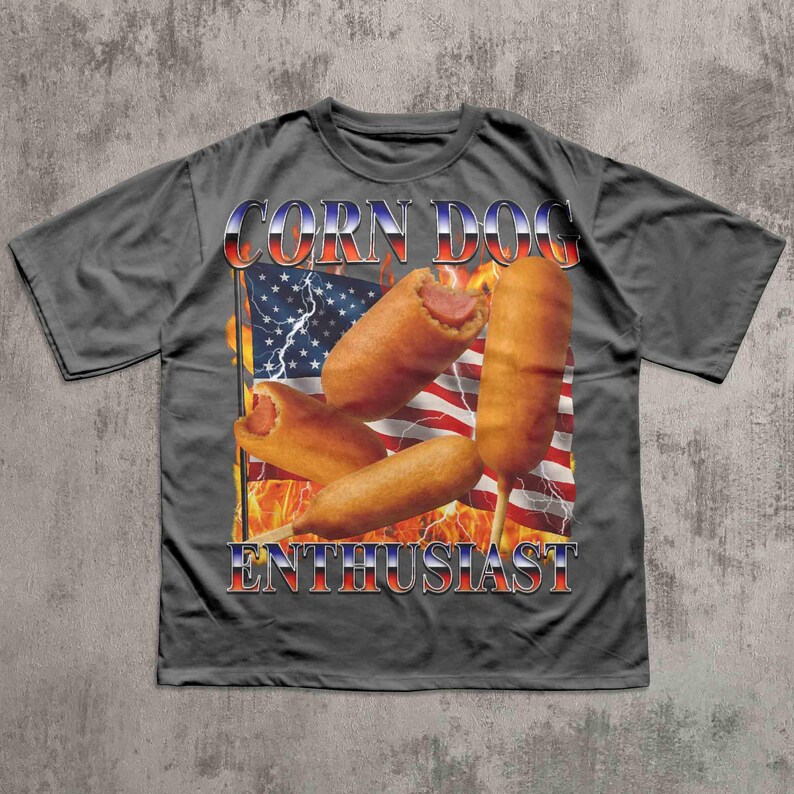 Op de afbeelding: Een grijs t-shirt met een afbeelding van corn dogs voor een Amerikaanse vlag met vlammen. De tekst "CORN DOG ENTHUSIAST" wordt weergegeven in een rood, wit en blauw lettertype.