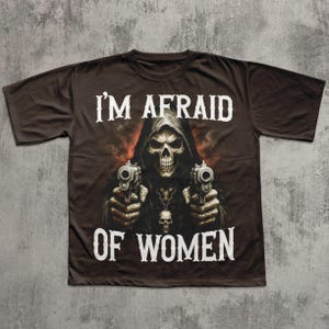 May include: Dark brown t-shirt featuring a grim reaper graphic holding two pistols. The text "I'M AFRAID OF WOMEN" is printed in white above and below the graphic. The shirt has a crew neck and short sleeves.