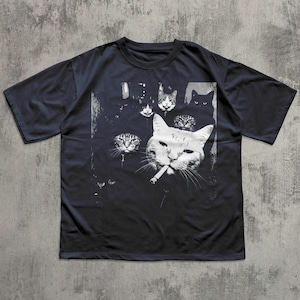 May include: Dark navy blue t-shirt featuring a black and white graphic of several cat faces, with one cat smoking a cigarette. The design has a vintage, slightly distressed look, with a grunge aesthetic.