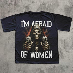 May include: Black t-shirt featuring a grim reaper graphic holding two pistols. The reaper is depicted with a skull face and a hooded cloak. The text "I'M AFRAID OF WOMEN" is printed in white.