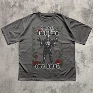 Könnte beinhalten: Graues T-Shirt mit einem mittelalterlichen Ritter, der Hanteln hebt, mit dem Text "Good sir dost thou even hoist?" umrahmt von Rosen und Weinranken. Das Design ist in Schwarz und Rot gehalten.