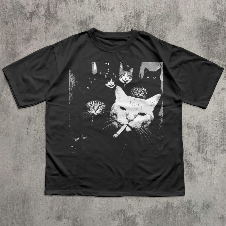 May include: Black t-shirt featuring a graphic of several cats, with one large white cat smoking a cigarette. The other cats are in the background, with various expressions. The design is in black and white.