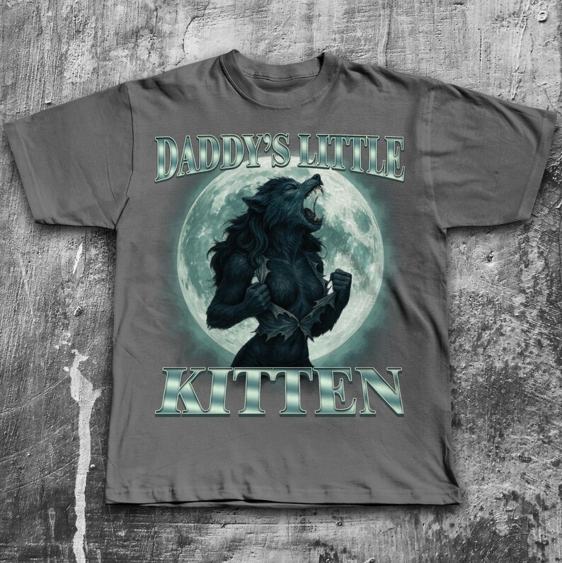 Pode incluir: Camiseta cinza com um gr&aacute;fico de lobisomem em frente a uma lua cheia. O texto "DADDY'S LITTLE KITTEN" &eacute; impresso acima e abaixo do gr&aacute;fico em uma fonte met&aacute;lica prateada. O lobisomem est&aacute; rasgando sua camisa.