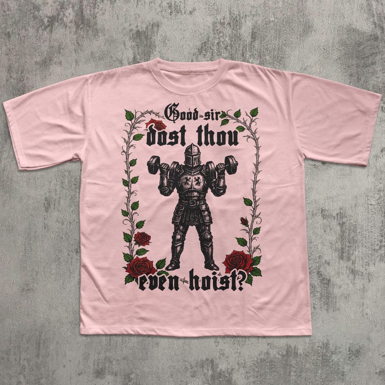 May include: A light pink t-shirt featuring a medieval knight lifting dumbbells. The knight is surrounded by a floral design with the text "Good sir dost thou even hoist?" in a gothic font. The shirt is made of a soft material.