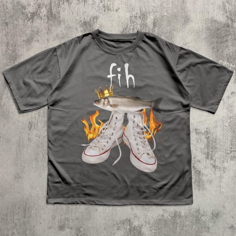 May include: Dark gray t-shirt featuring a graphic design. The design includes a fish wearing a crown above a pair of white sneakers with flames. The word "fih" is printed above the fish in white.