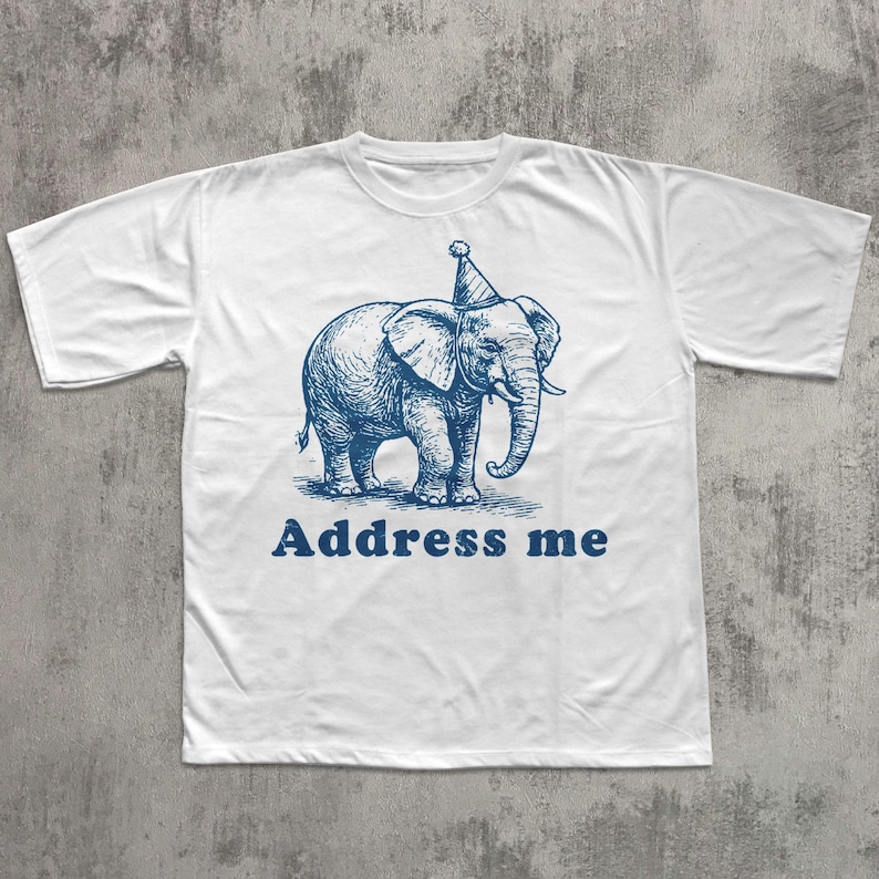 May include: White t-shirt with a blue illustration of an elephant wearing a party hat. The text "Address me" is printed below the elephant. The shirt is made of a soft material.
