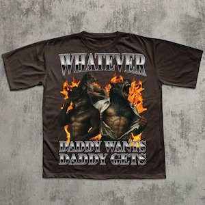 May include: Brown t-shirt featuring the text "WHATEVER" above a graphic of two werewolves in front of flames. The text "DADDY WANTS DADDY GETS" is below the graphic.