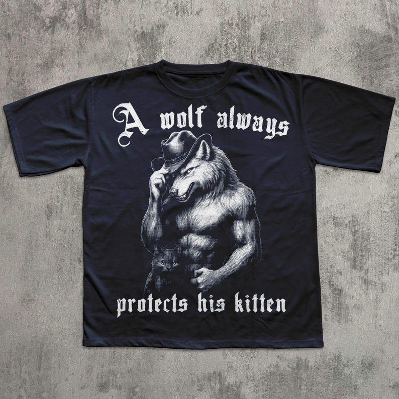 May include: Black t-shirt featuring a muscular wolf wearing a hat, holding a kitten. The text "A wolf always protects his kitten" is printed in white, gothic-style font above and below the wolf illustration.