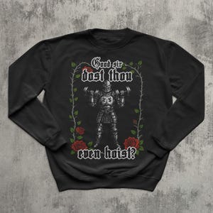 Pode incluir: Camisola preta com um cavaleiro de armadura a levantar halteres. O texto "Good sir dost thou even hoist?" está escrito numa fonte decorativa. O design inclui rosas vermelhas e videiras verdes.