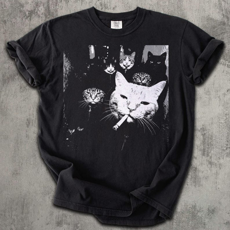 May include: Black t-shirt featuring a black and white graphic of several cats. One large cat in the foreground is smoking a cigarette. The other cats are in the background.
