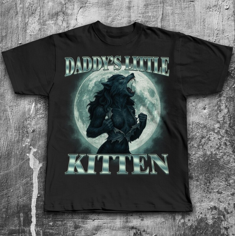 Pode incluir: Camiseta preta com uma ilustra&ccedil;&atilde;o de lobisomem em frente a uma lua cheia. O texto "DADDY'S LITTLE KITTEN" &eacute; exibido acima e abaixo do gr&aacute;fico em uma fonte prateada e met&aacute;lica. O lobisomem &eacute; retratado com uma express&atilde;o carrancuda.