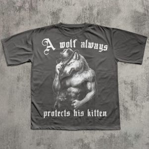 May include: Dark gray t-shirt featuring a muscular wolf wearing a cowboy hat. The wolf illustration is in black and white. The text "A wolf always protects his kitten" is in white, gothic-style font.