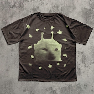 Puede incluir: Camiseta marr&oacute;n con un dise&ntilde;o de cara alien&iacute;gena y estrellas de color verde claro. El gr&aacute;fico es una impresi&oacute;n de semitonos. La camiseta tiene mangas cortas y cuello redondo. La camiseta es de material suave.