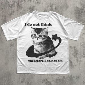 May include: White t-shirt featuring a black and white graphic of a kitten encircled by a crescent and star. The text "I do not think" is above the kitten, and "therefore I do not am" is below.
