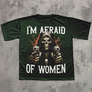 May include: Dark green t-shirt featuring a grim reaper graphic holding two pistols. The text "I'M AFRAID OF WOMEN" is printed in white across the top and bottom of the image. The design has a skull and flames.