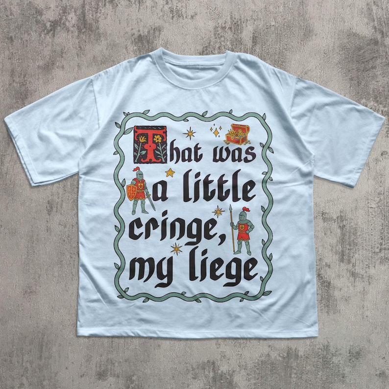 Puede incluir: Una camiseta azul claro con un estampado gr&aacute;fico y un borde decorativo de enredadera verde. El texto dice "That was a little cringe, my liege", acompa&ntilde;ado de ilustraciones de dos caballeros, un cofre del tesoro y peque&ntilde;as estrellas.