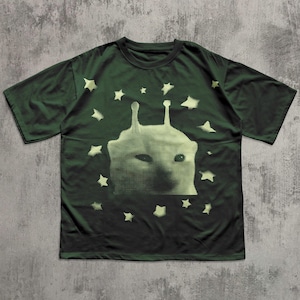Puede incluir: Camiseta verde oscuro con una criatura extraterrestre verde claro y estrellas. El gr&aacute;fico es un dise&ntilde;o de semitonos. La camiseta tiene mangas cortas y cuello redondo.