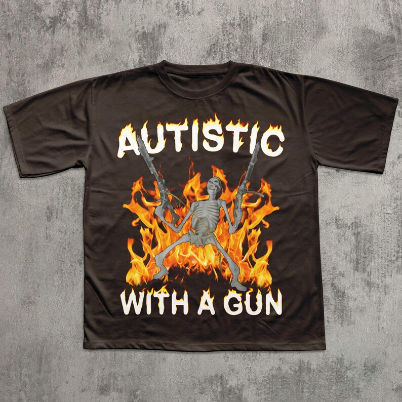 May include: Dark brown t-shirt with the words "AUTISTIC" and "WITH A GUN" in white. The graphic features a skeleton figure holding two guns, set against a backdrop of flames.
