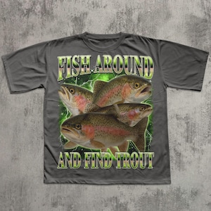 May include: Gray t-shirt featuring a graphic of four trout fish with the text "FISH AROUND AND FIND TROUT" in green and white. The fish have red and brown markings.