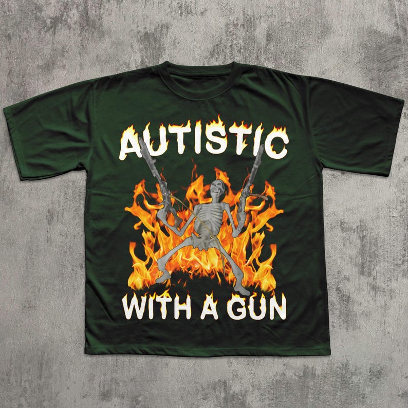 May include: Dark green t-shirt with the text "AUTISTIC WITH A GUN" in white, featuring a skeleton holding two guns in front of a fiery background. The shirt is a crew neck style.