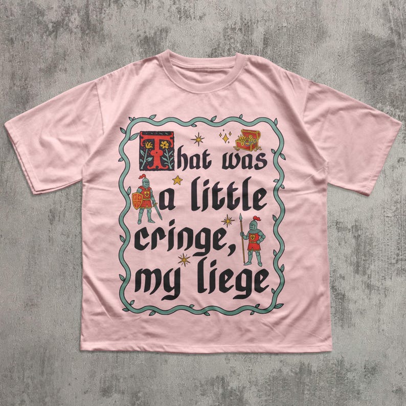 Puede incluir: Una camiseta de manga corta de color rosa claro con un gr&aacute;fico central rodeado por un borde de enredadera verde. El dise&ntilde;o incluye dos caballeros, un cofre del tesoro, estrellas y el texto negro "That was a little cringe, my liege" con una T roja.