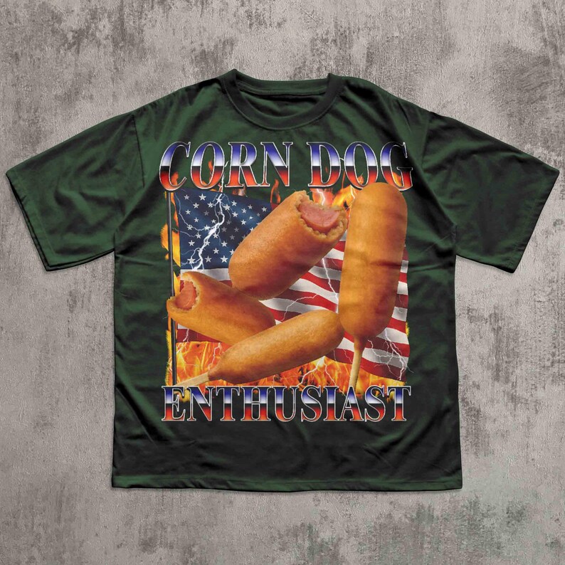 Op de afbeelding: Donkergroen t-shirt met een afbeelding van corn dogs voor een Amerikaanse vlag met vlammen en bliksem. De tekst "CORN DOG ENTHUSIAST" staat in rood, wit en blauw.