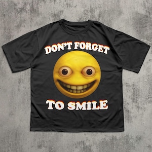 May include: Black t-shirt featuring a large yellow emoji with a wide grin and bulging eyes. The text "DON'T FORGET TO SMILE" is printed above and below the emoji in white, outlined in red.
