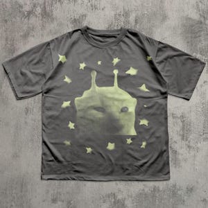 Puede incluir: Camiseta gris oscuro con un dise&ntilde;o de criatura alien&iacute;gena verde claro y estrellas. El gr&aacute;fico es una impresi&oacute;n de semitonos. La camiseta tiene cuello redondo y mangas cortas. La camiseta es de material suave.