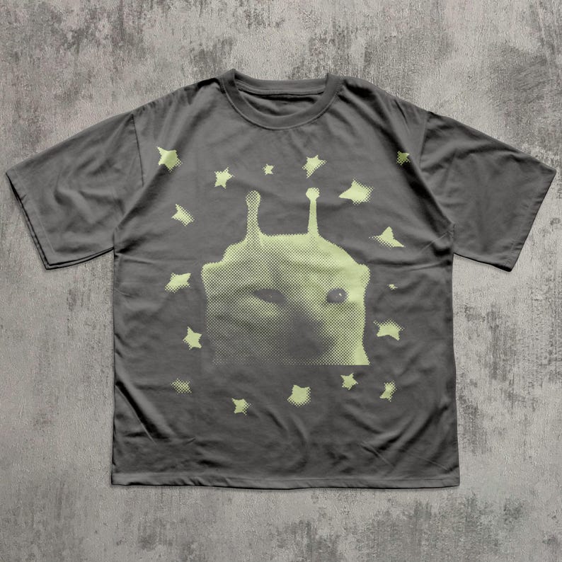 Puede incluir: Camiseta gris oscuro con un dise&ntilde;o de criatura alien&iacute;gena verde claro y estrellas. El gr&aacute;fico es una impresi&oacute;n de semitonos. La camiseta tiene cuello redondo y mangas cortas. La camiseta es de material suave.