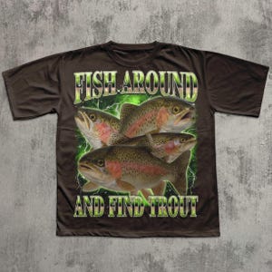 May include: Brown t-shirt featuring a graphic of four trout fish with the text "FISH AROUND AND FIND TROUT" in a green and white design. The fish have red and brown markings.