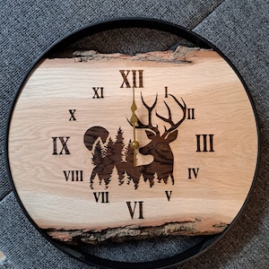 Peut inclure: Une horloge en bois avec un cadre en métal noir. Le cadran de l'horloge présente une silhouette de cerf dans une forêt avec des chiffres romains pour les heures. Les aiguilles de l'horloge sont dorées.