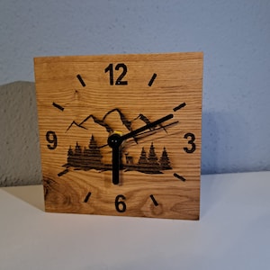 Puede incluir: Un reloj de madera con un diseño de montaña y bosque. La esfera del reloj tiene números y manecillas negros. El reloj está hecho de madera marrón claro.