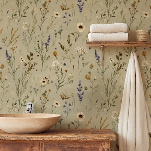 Könnte beinhalten: Badezimmer-Szene mit einem Holzwaschtisch und einem hellen, runden Waschbecken. Die Wand ist mit floraler Tapete in Grün-, Weiß- und Lilatönen geschmückt. Ein Holzregal hält gefaltete Handtücher und einen kleinen geflochtenen Korb. Ein weißes Handtuch hängt darunter.