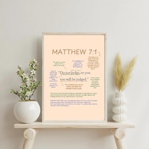 Puede incluir: Una impresión enmarcada con el texto "Mateo 7:1" y la cita "No juzguéis, para que no seáis juzgados." La impresión tiene un fondo de color melocotón claro y se muestra en una estantería de madera con jarrones y plantas decorativas.